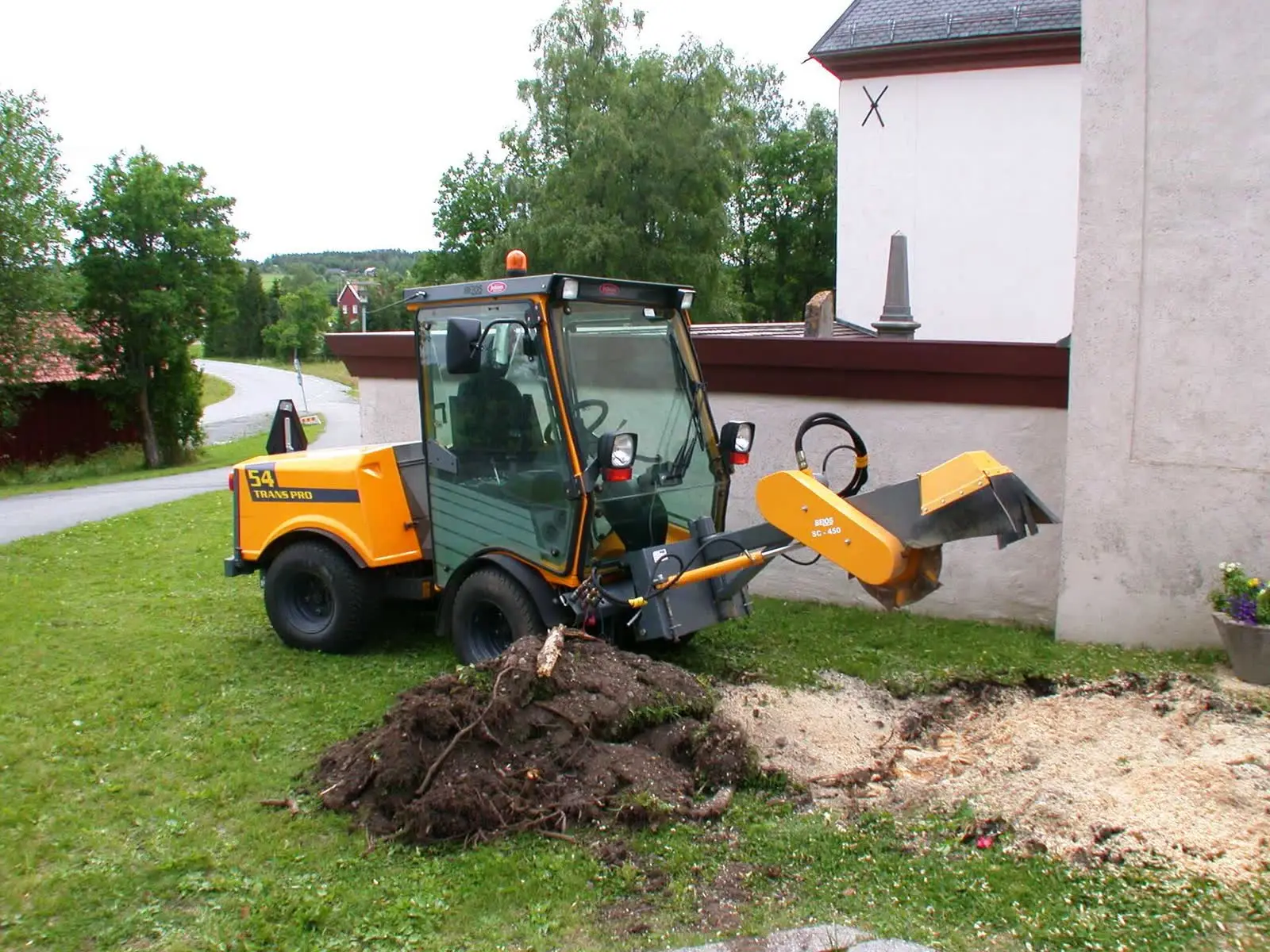 A compact stump grinder working beside a building wall