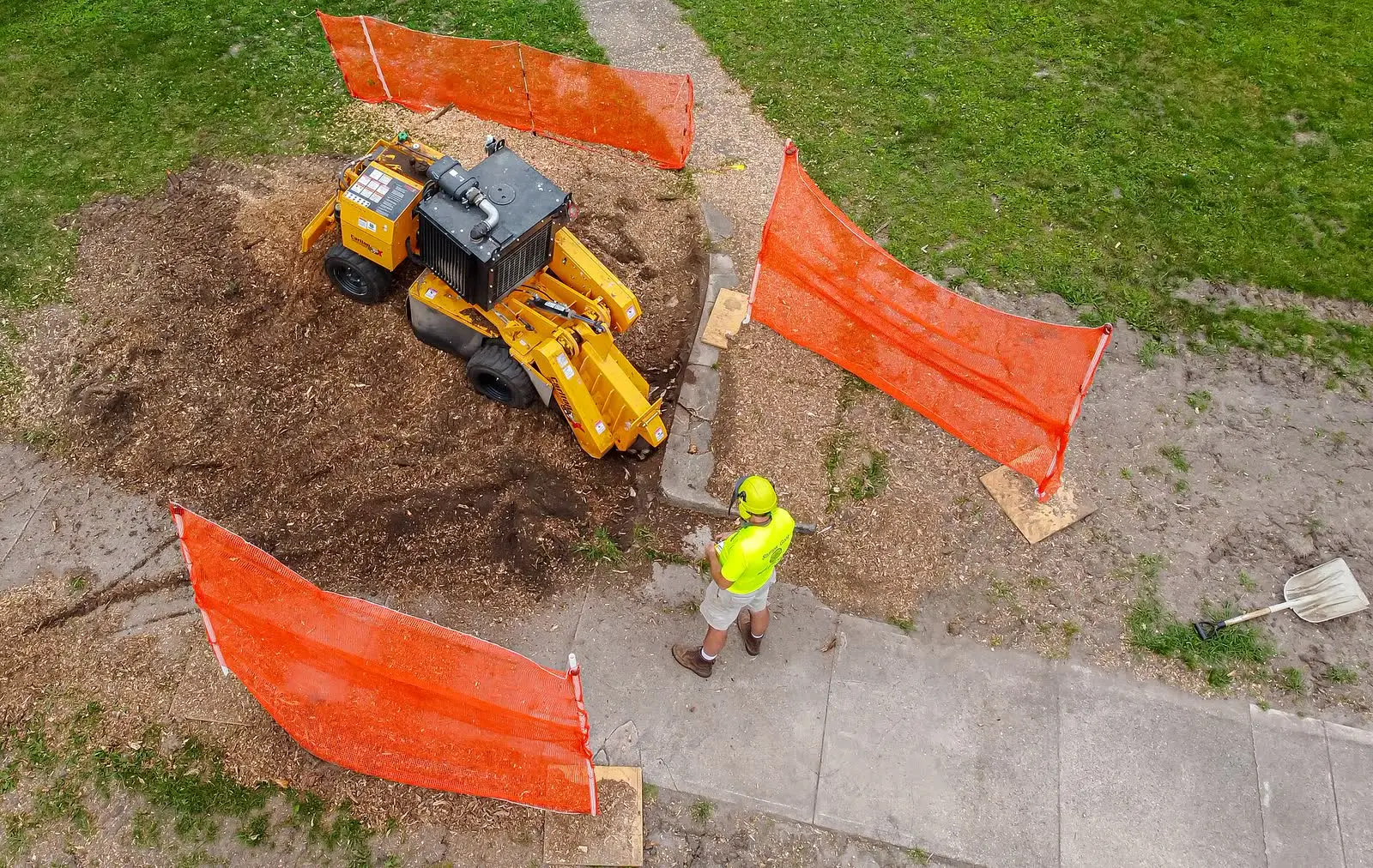 A stump grinder working inside orange debris screens on a lawn
