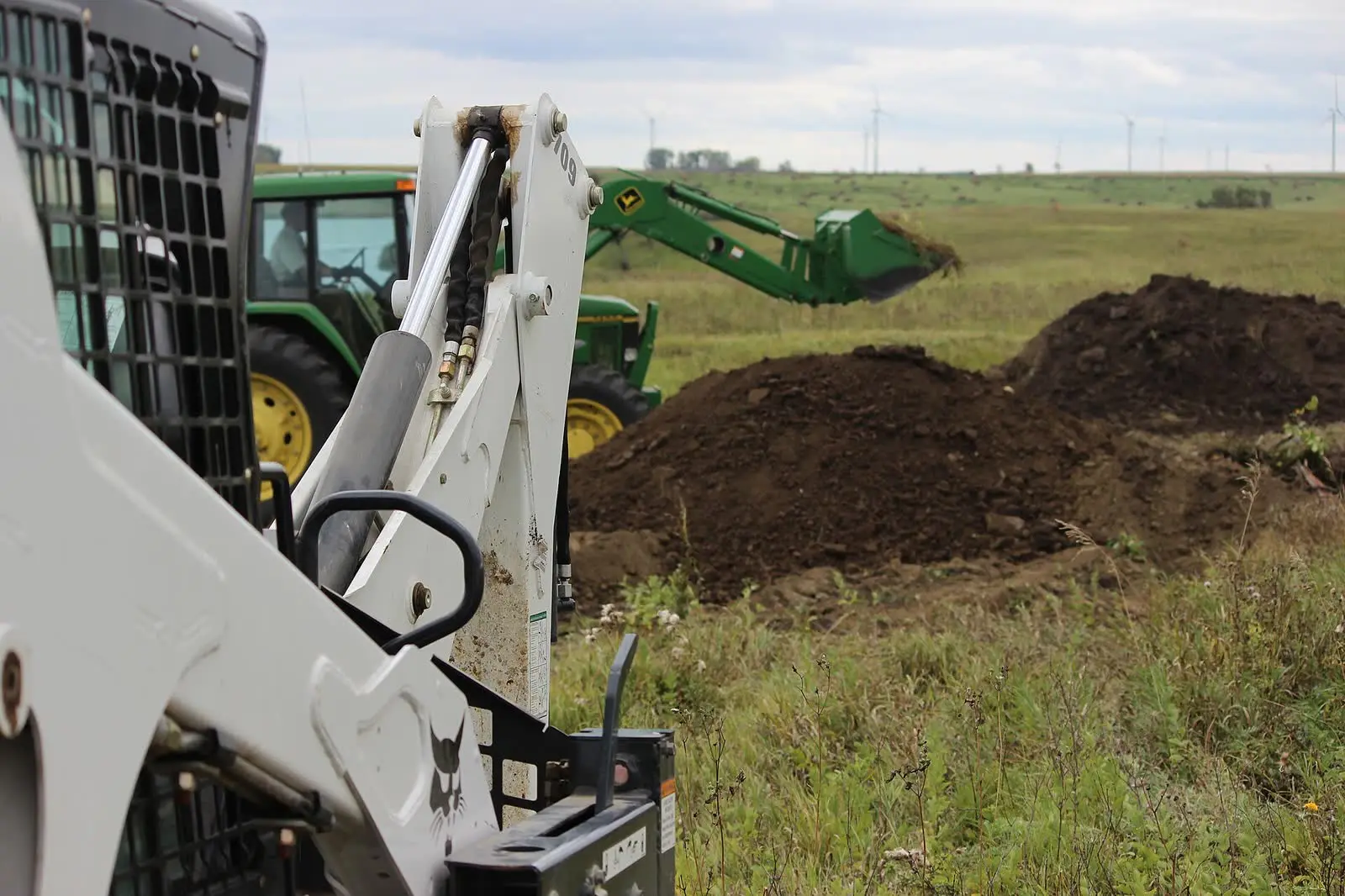 A skid steer loader and a tractor moving a pile of excavated soil